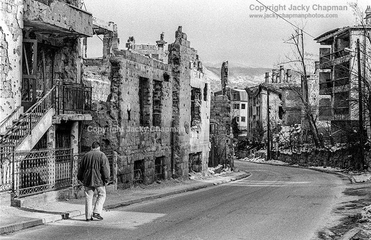 A country destryed. A man strolls by bombed out buildings near the front line, Grbavica, Sarajevo.